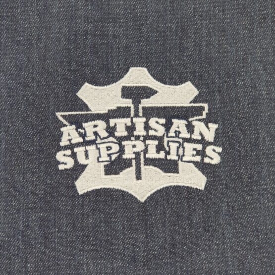 Close up of the white logo embroidered on the front of the Artisan Supplies Denim Apron